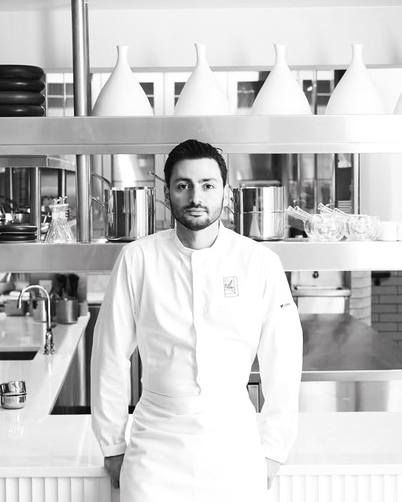 Black-and-white portrait of chef Andrea Clastier in his professional restaurant kitchen