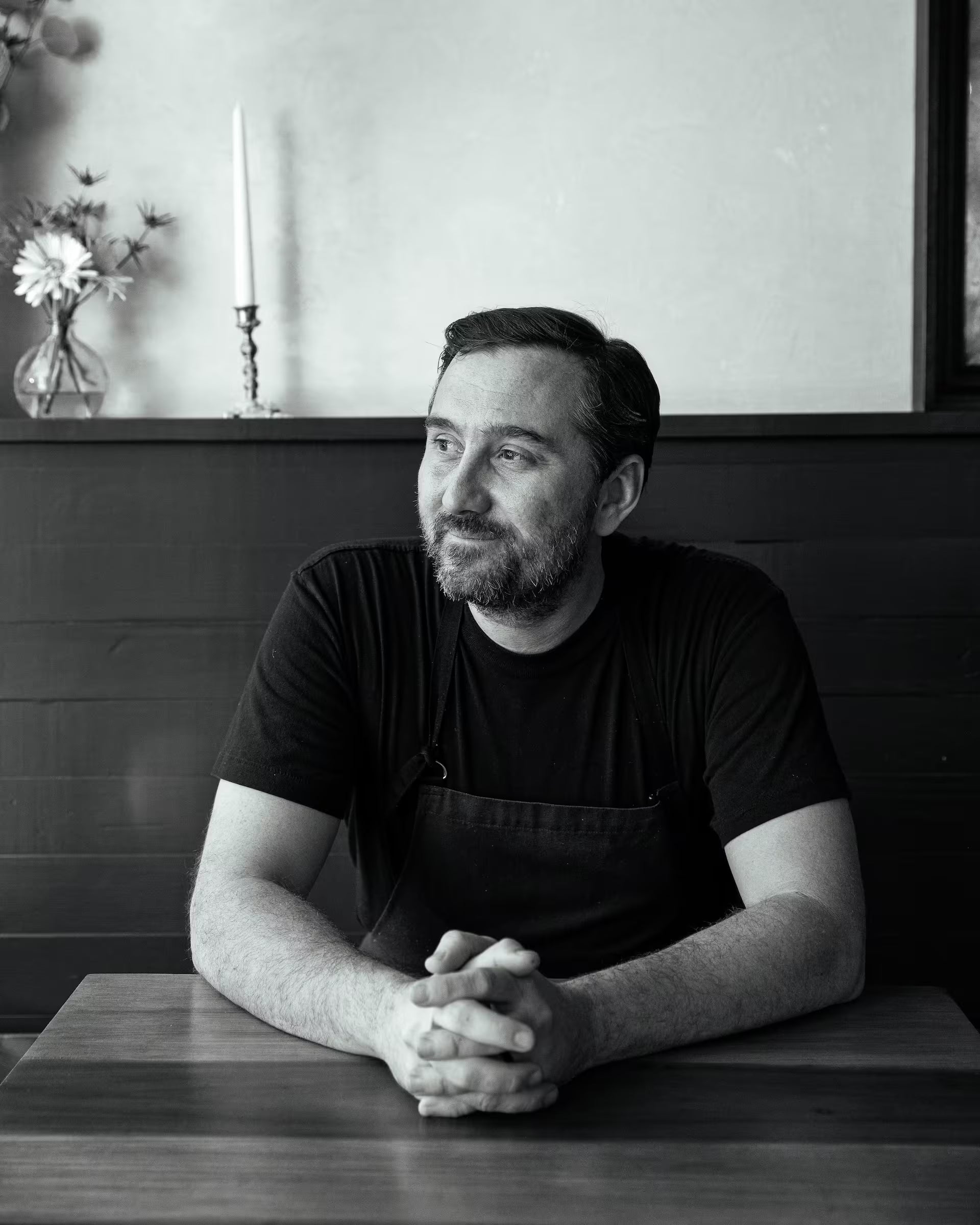 Black-and-white portrait of chef Dano Heinze seated at a restaurant table, hands clasped