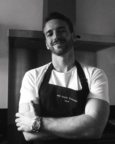 Black-and-white portrait of chef Juan Fortunato in an embroidered apron, arms crossed