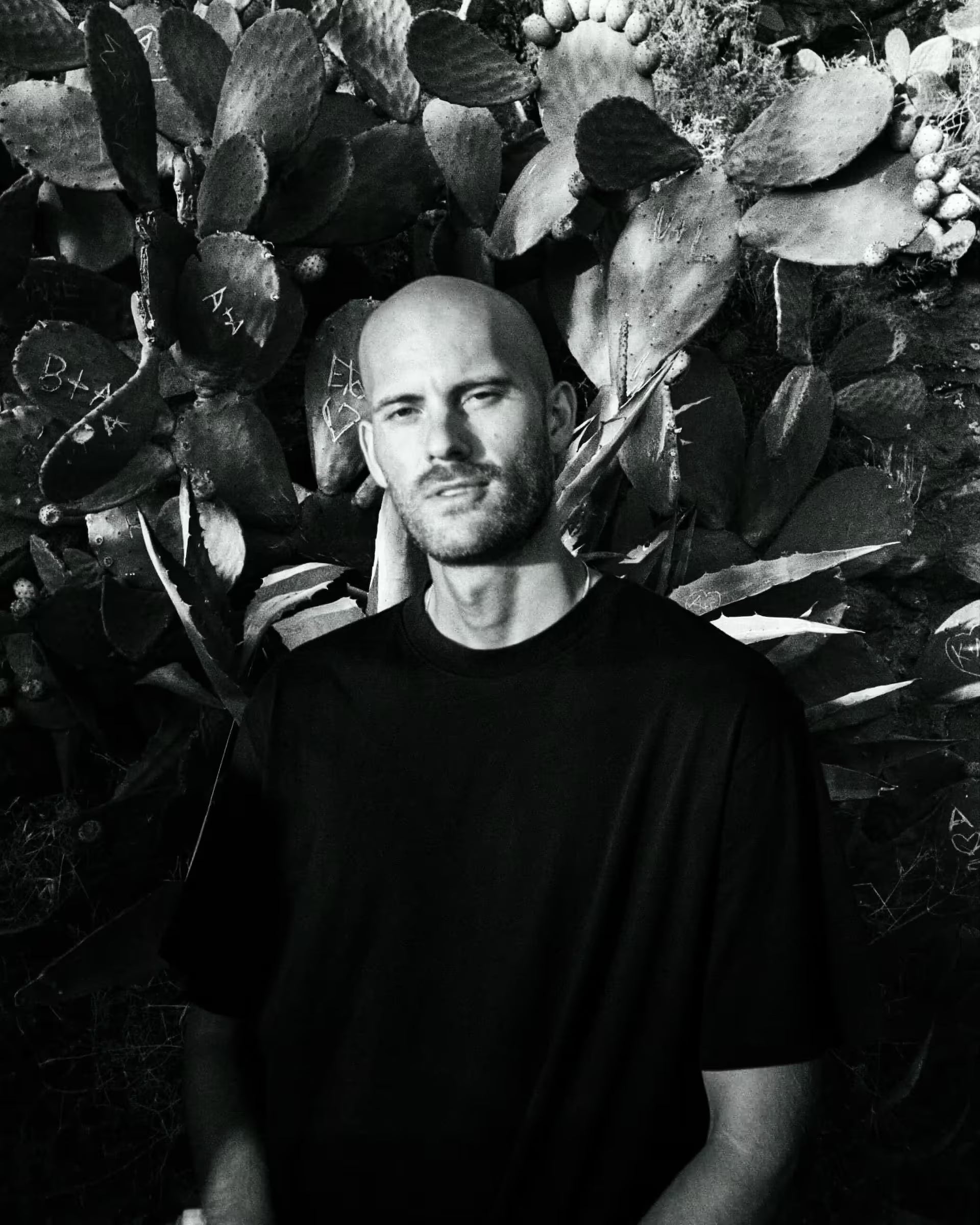Black-and-white portrait of chef Max Jarmey standing in front of a wall of prickly pear cacti