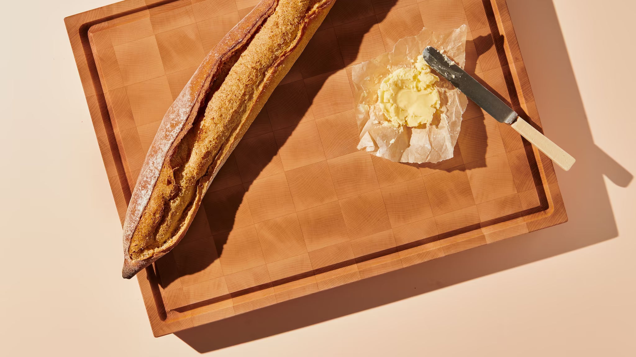 Maison Liverani maple end-grain cutting board with a whole baguette and butter on parchment