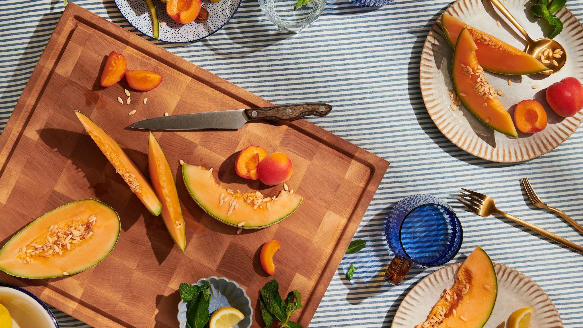 Maple end-grain cutting board with sliced cantaloupe and apricots on a sunlit summer table