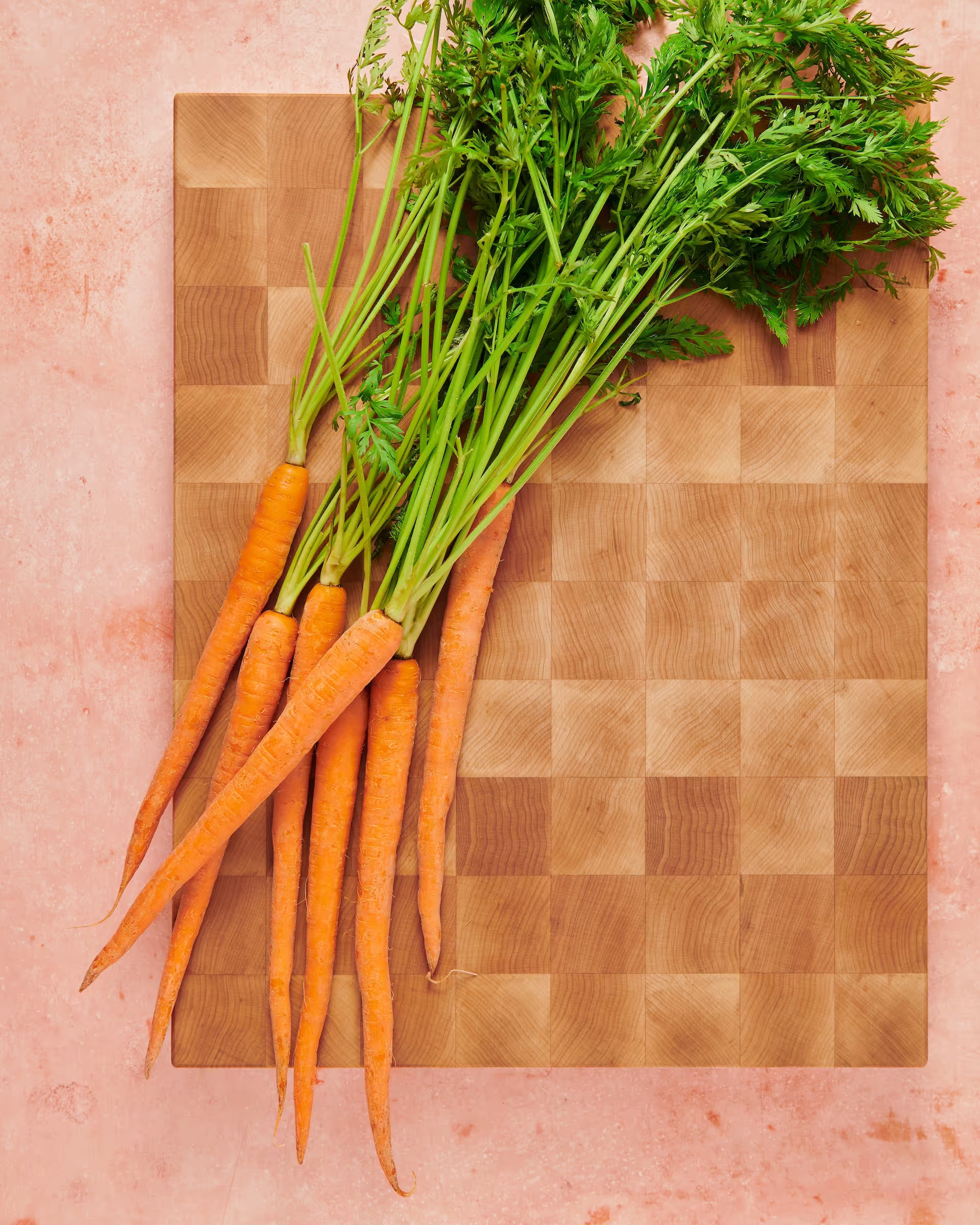 Maple end-grain cutting board topped with a bunch of fresh carrots and their green tops