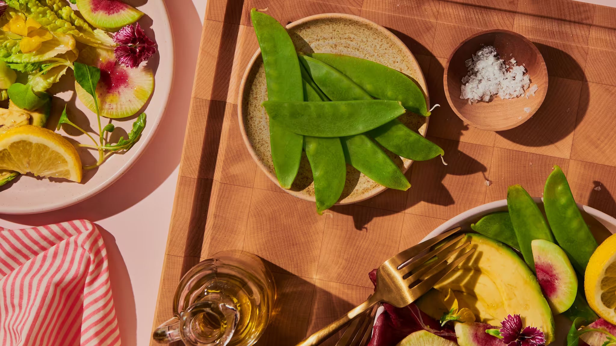 Maple end-grain cutting board with a plate of snow peas and flaky salt in sunlight