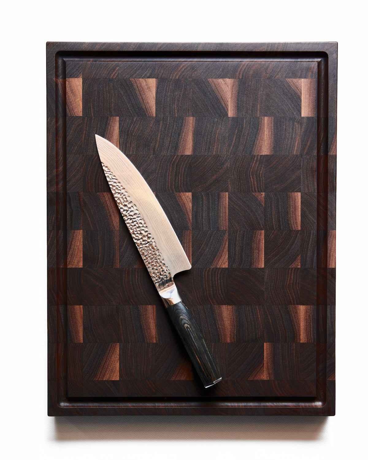 Chef’s knife resting diagonally on a walnut Maison Liverani cutting board with juice groove