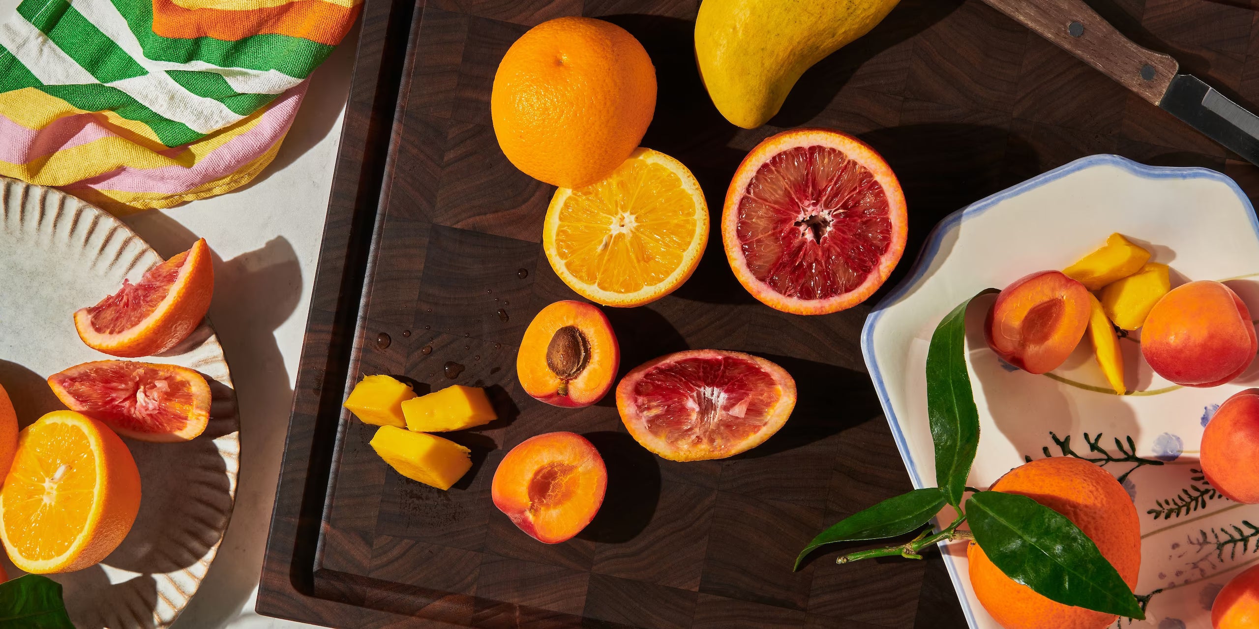 Maison Liverani walnut end-grain cutting board with sliced blood oranges, apricots, and mango in bright sunlight