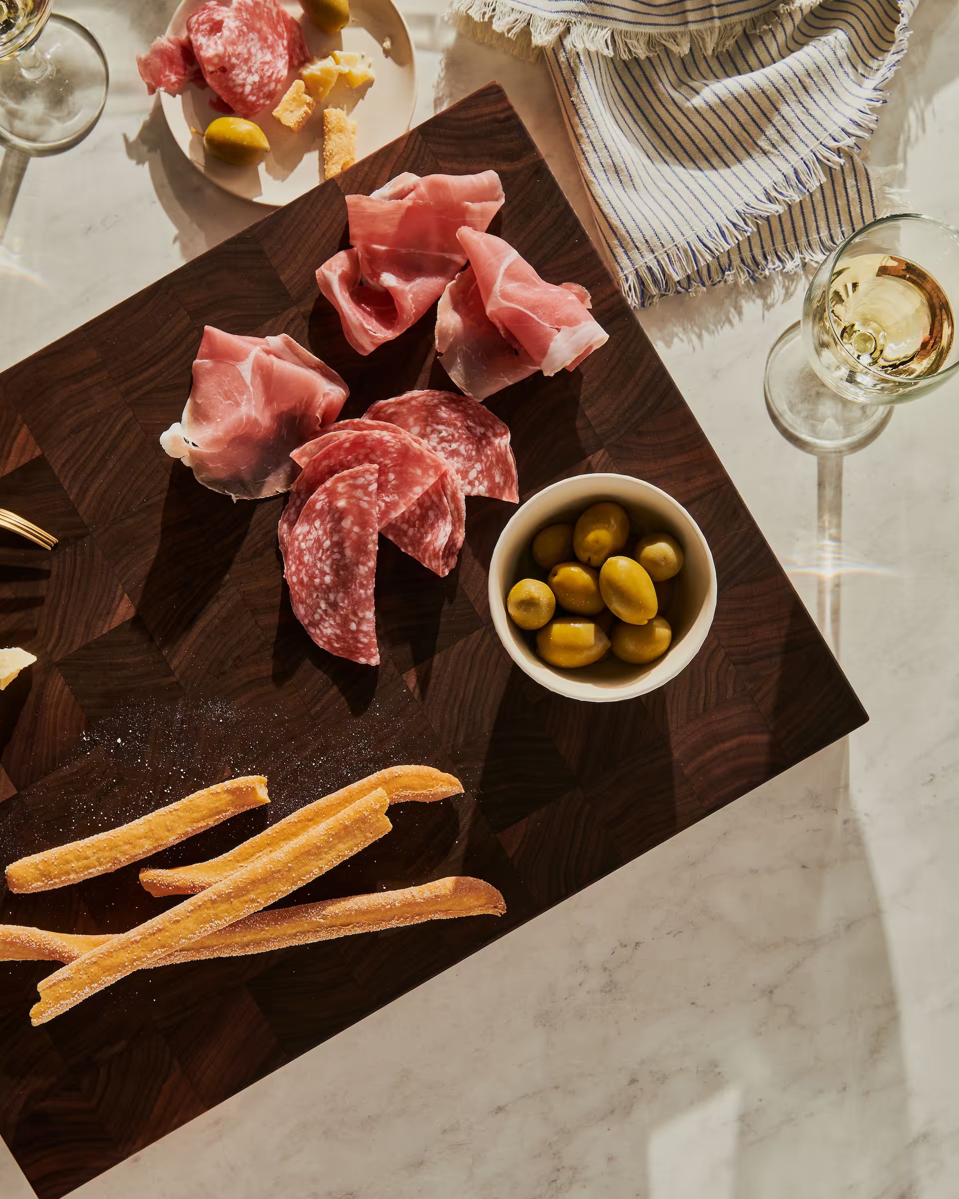 Walnut end-grain serving board with prosciutto, salami, green olives, and breadsticks