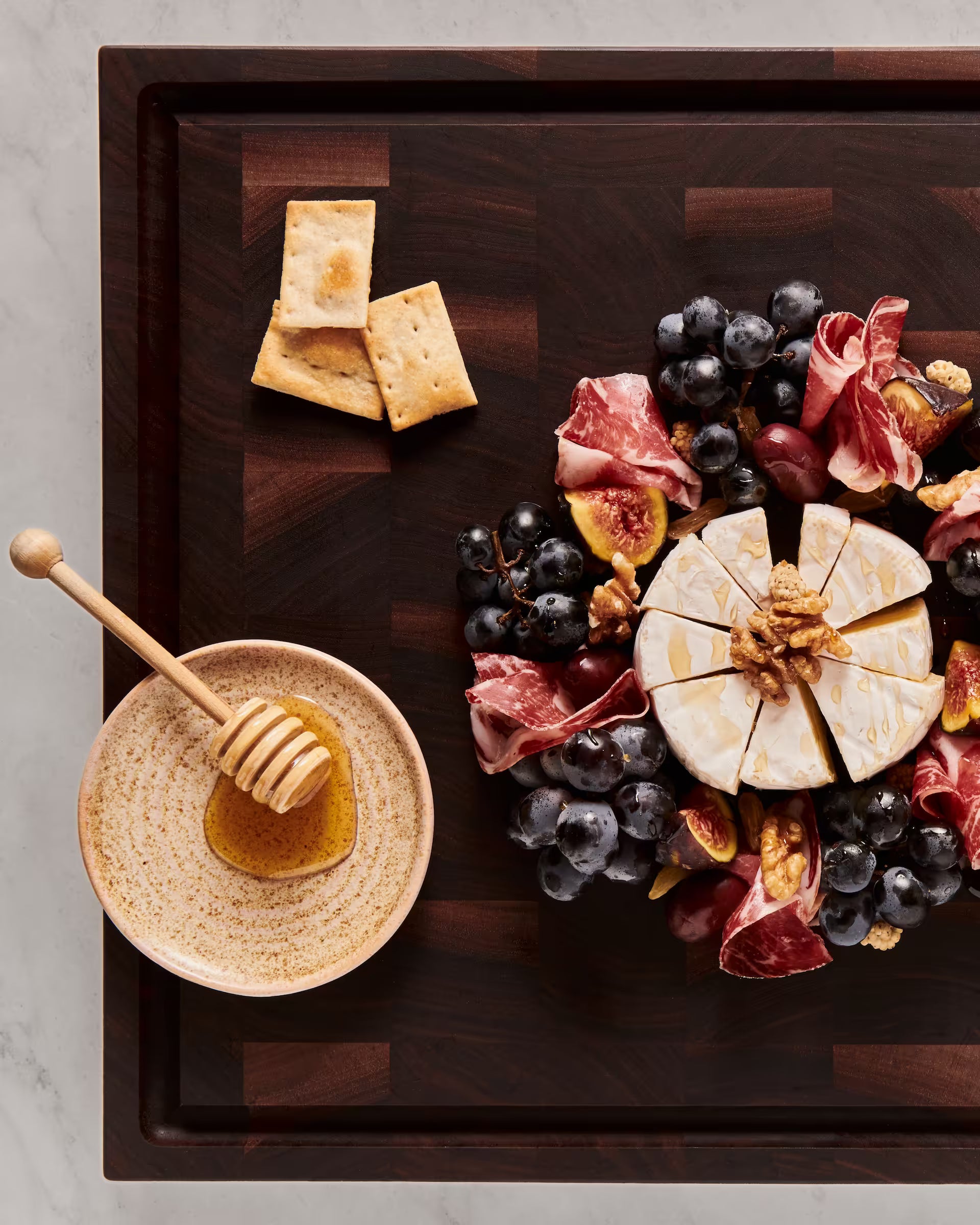 Walnut end-grain serving board with brie, grapes, figs, cured meat, and honey